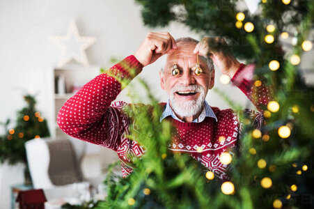senior-man-standing-by-christmas-tree-putting-balls-in-front-of-his-eyes-HPIF29296.jpg