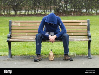 male-wearing-hoodie-sitting-on-park-bench-drinking-alcohol-DY1T8D.jpg