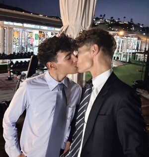 Two young men in snug shirts and ties kissing on the lips.jpeg